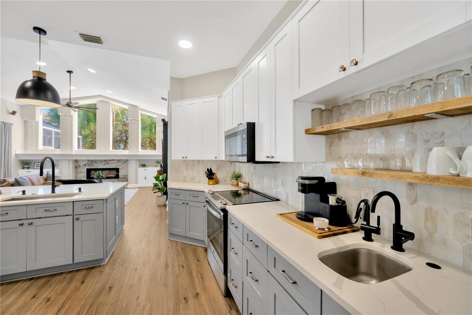 Kitchen is equipped with stylish open wood-stained shelving, and a convenient second bar-sized sink and disposal with a filtration system offering instant hot water making it the perfect coffee bar.