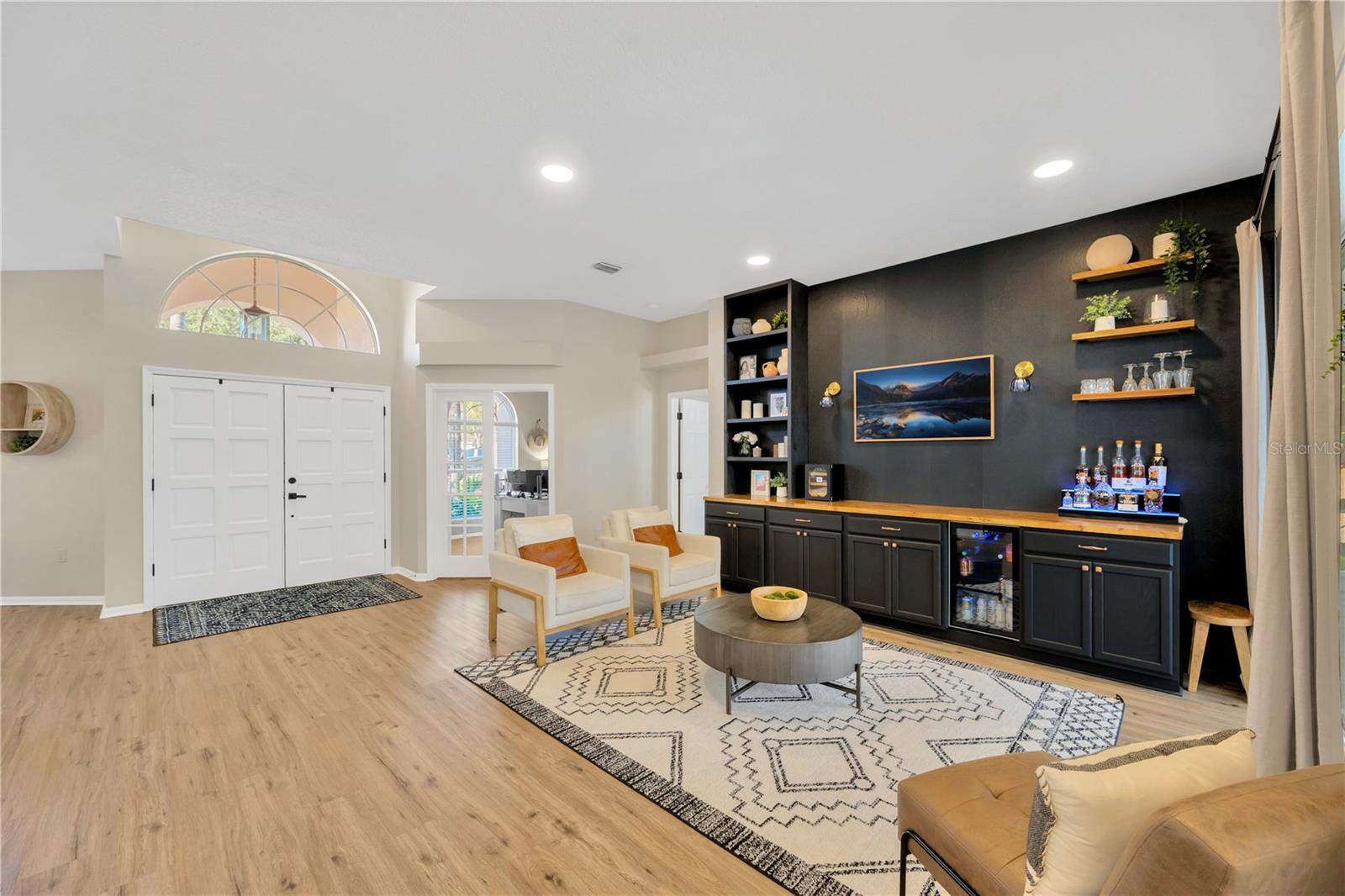 View of the living room and the double entry front door, private office and entrance into the primary suite beyond featuring elevated luxury vinyl plank flooring