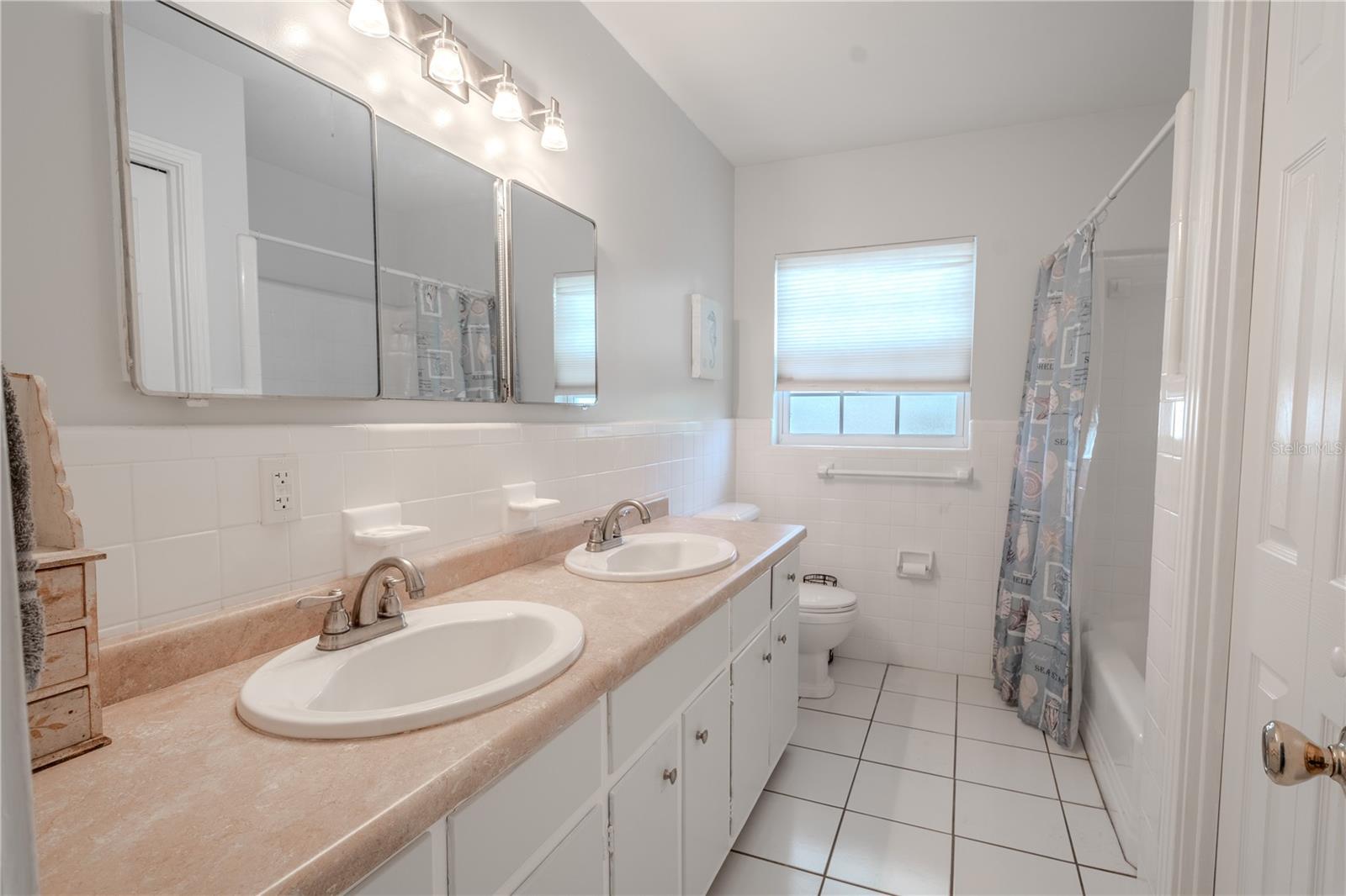 Bathroom 2 features a mirrored, dual sink vanity with storage, ceramic tile floor and a tub with shower.