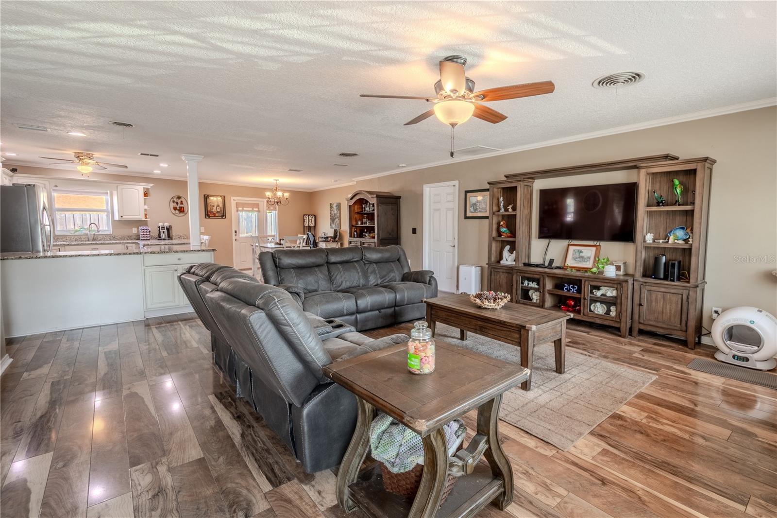 The open floor plan features a spacious living room in neutral tones, a wood floor, and ceiling fan with light kit.