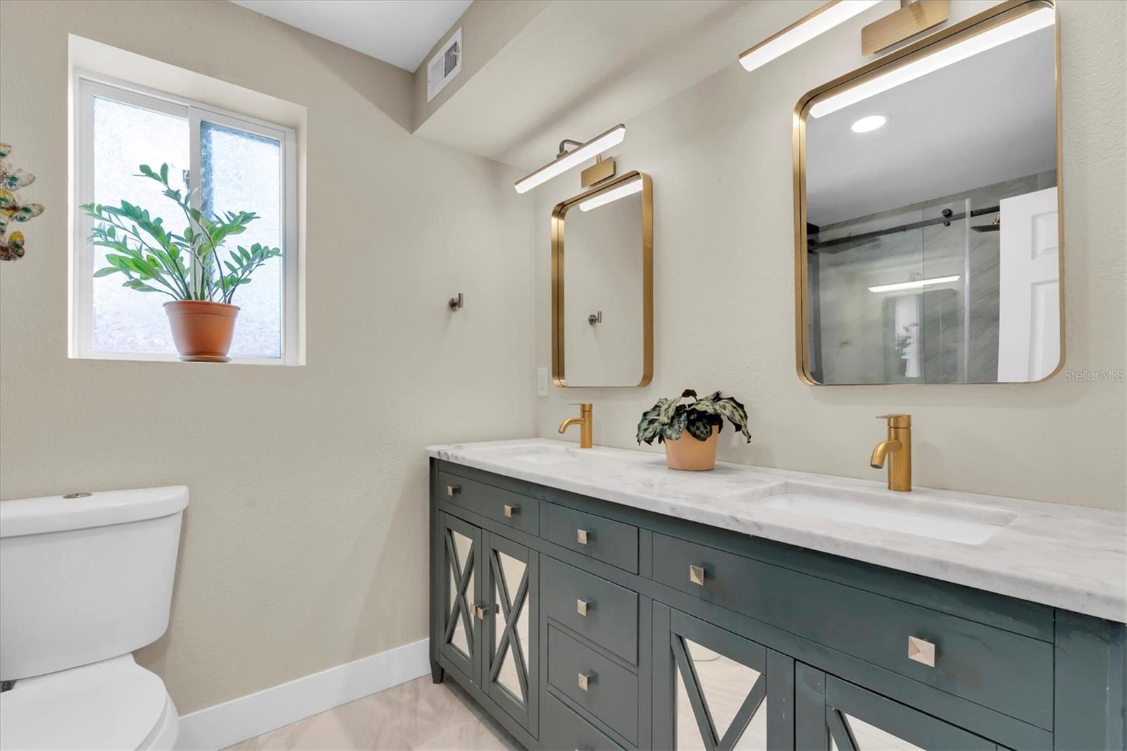 Primary en-suite bathroom features granite countertops, double vanities, a tiled walk-in shower with double rainfall shower heads, glass shower doors and ceramic tile flooring.