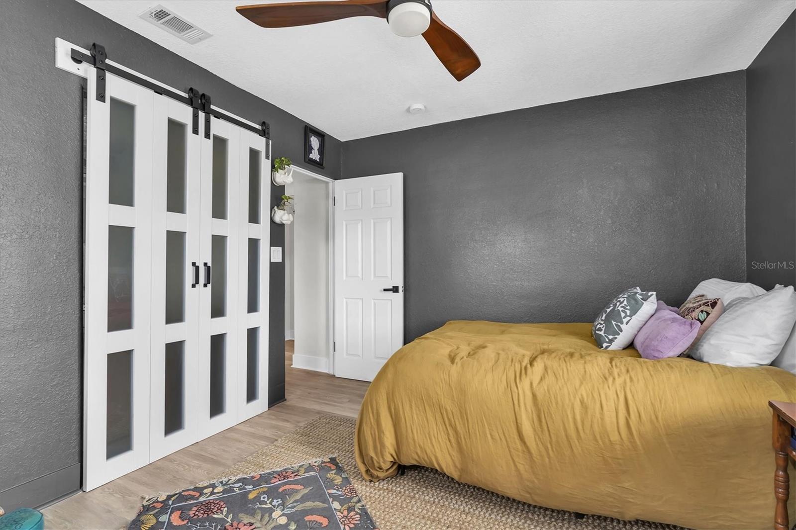 Second Bedroom  has luxury vinyl tile, ceiling fan, custom blinds, and lovely bi-fold barn doors.  This  split floor plan is ideal for family, guests, or home office space.