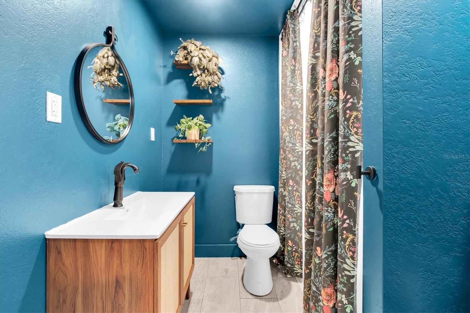 Spacious second bathroom conveniently located between bedrooms 2 and 3 boasts a tiled tub shower combo, floating shelves, large vanity, and ceramic tile flooring.