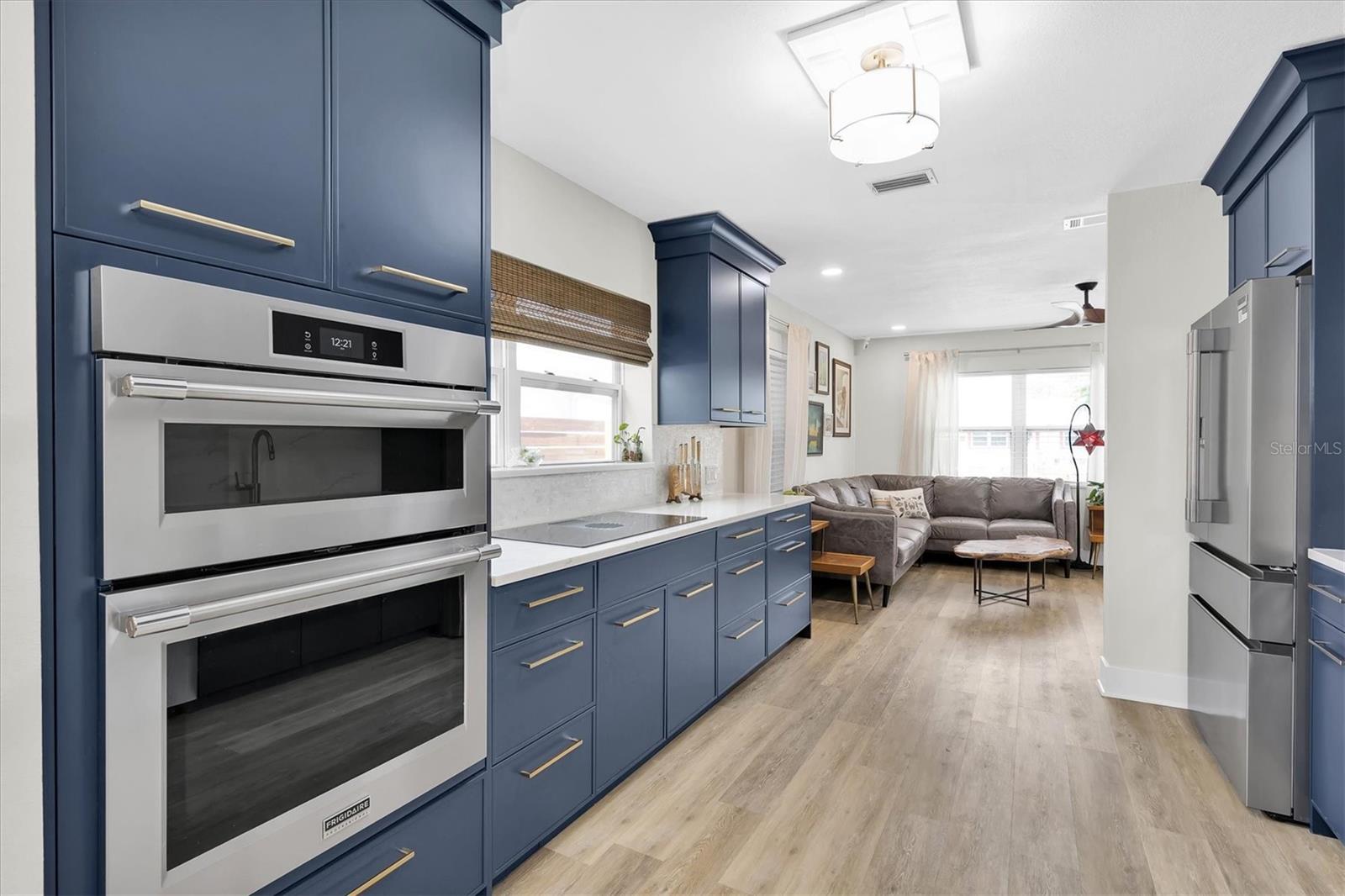 New stainless steel appliances, including a counter-depth refrigerator with convertible freezers, a wall oven/microwave combo with air fryer, a dishwasher conveniently located next to the large one bowl sink with touchless smart kitchen faucet, and a 36" induction cooktop with external downdraft. Gorgeous solid quartz countertops and seamless Mother of Pearl backsplash perfectly complement the blue wood cabinets.