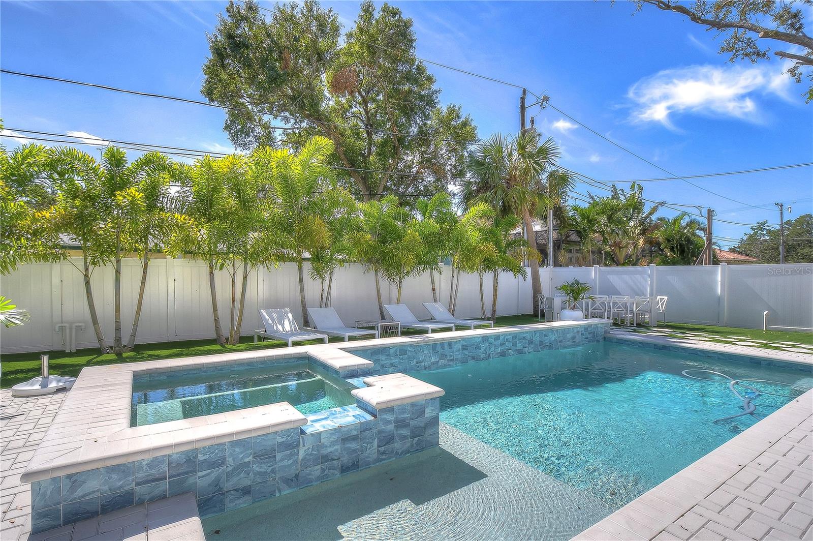 Dive into pure luxury with this exquisite backyard oasis, featuring a sparkling pool and hot tub surrounded by lush palm trees.