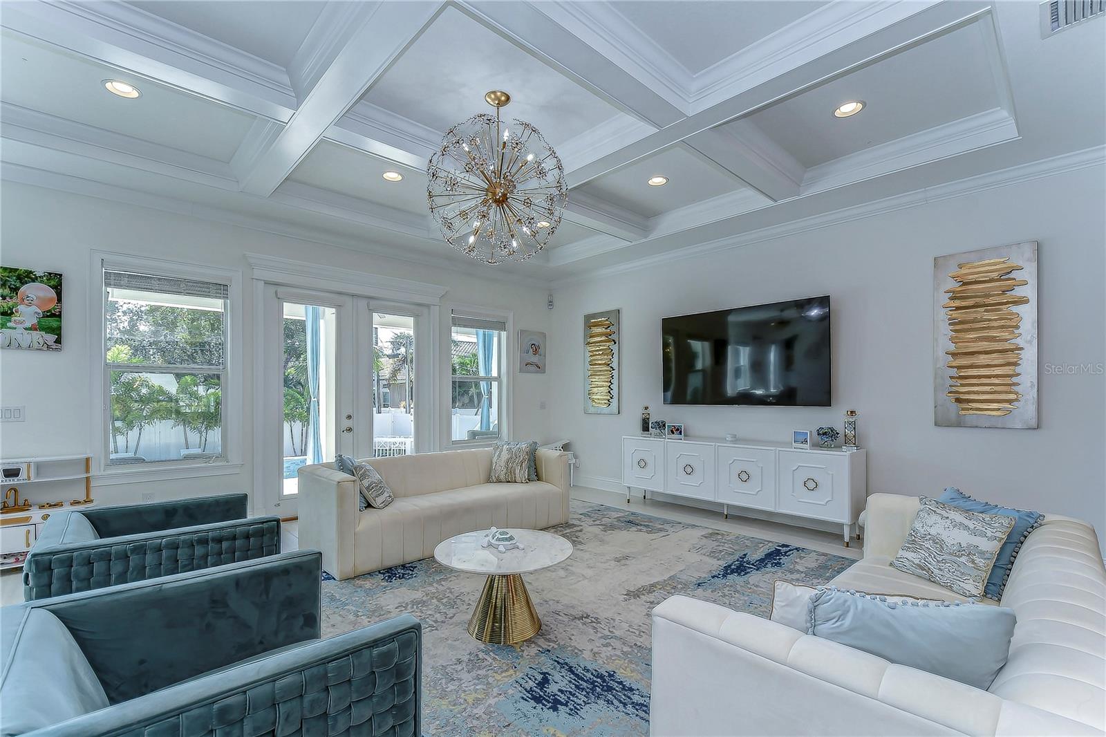 This elegant living room is a symphony of light, boasting an opulent chandelier and coffered ceilings that echo sophistication.