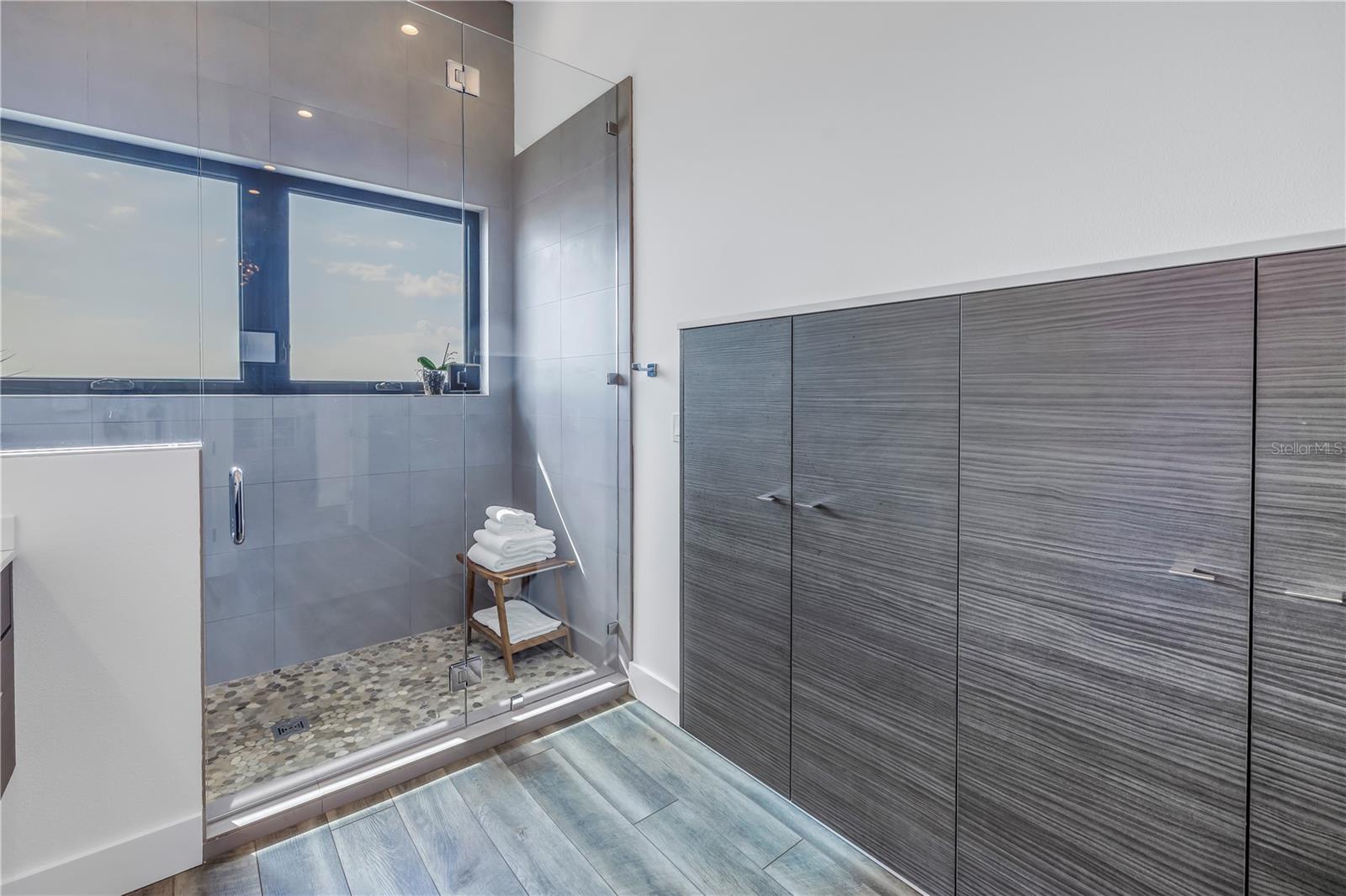 Shower and plenty of custom cabinets in primary bathroom.