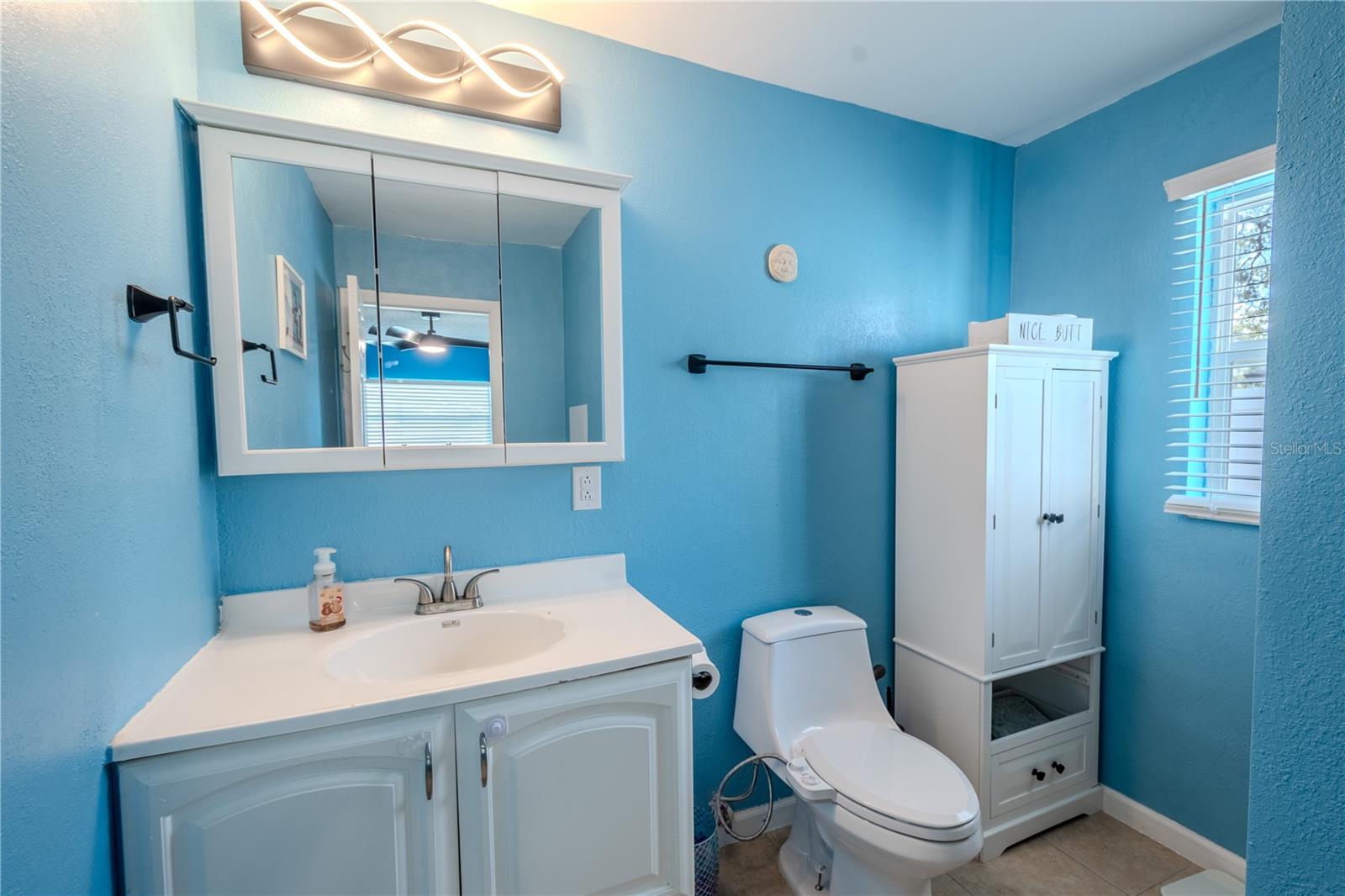 The primary ensuite bathroom features a mirrored vanity with storage, modern light fixture and ceramic tile floor.