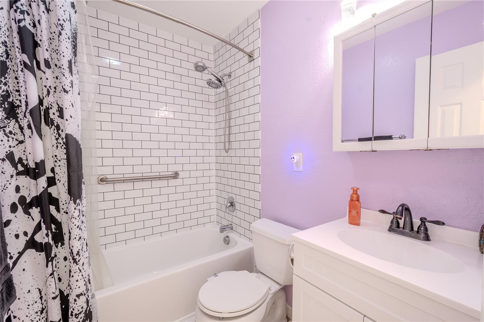 Bathroom 2 features a tub with shower enhanced with contemporary subway tile, a mirrored vanity with downlight light fixture and a tile floor.