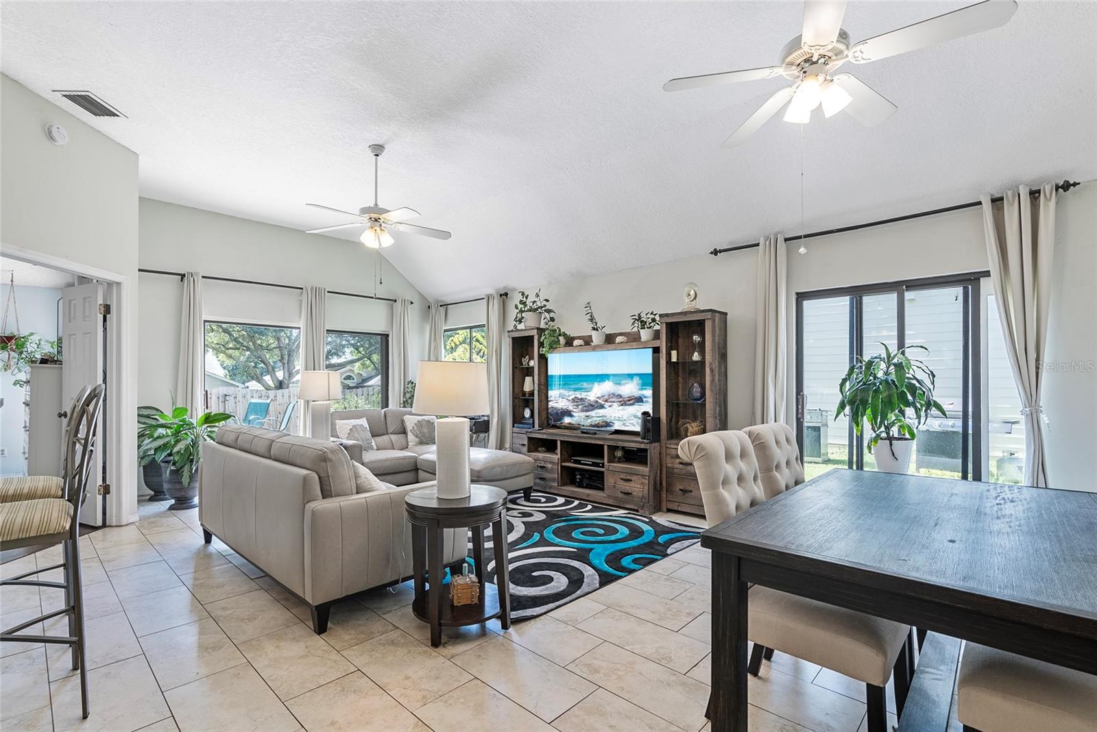 Photo of the living room/dining room from the foyer.  The primary bedroom entrance is in the background to the left.  The backyard can be accessed by a trio of sliding glass doors, including 2 from the living room & dining room and one from the primary bedroom.