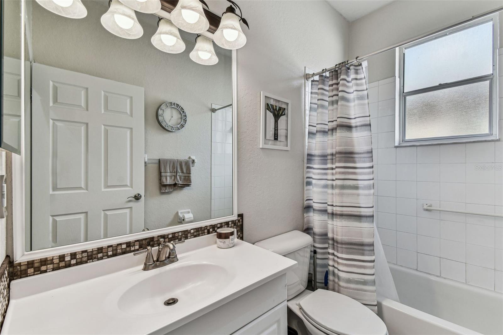 Second bath with tub and shower. Designer light fixture and backsplash.