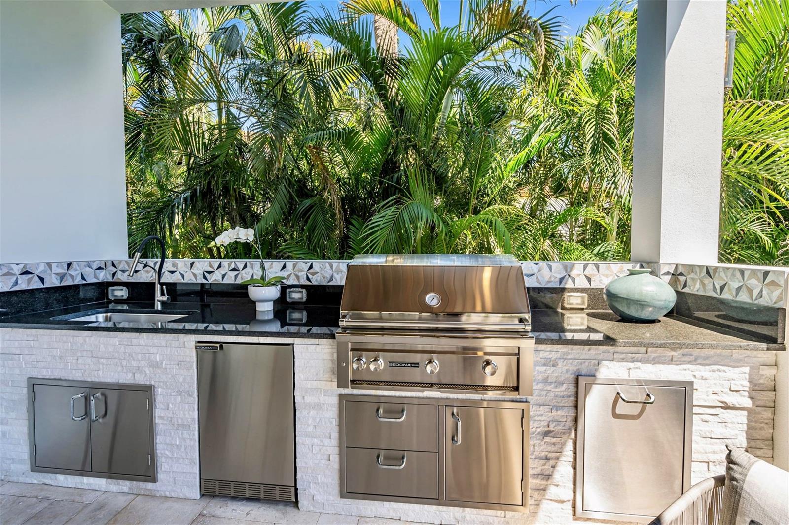 Summer kitchen featuring Sedona natural gas grill, refrigerator and sink with stone counter.