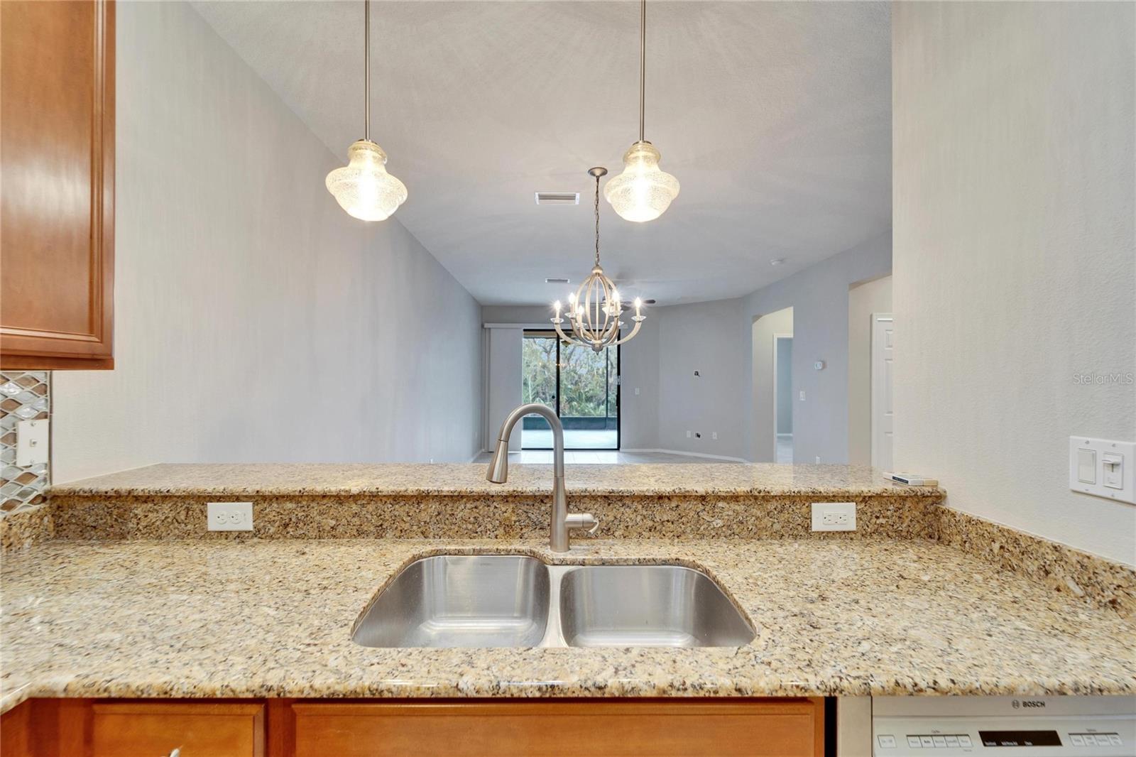 Double sink with view over breakfast bar and through greatroom/diningroom to the extended lanai with view of the nature path.