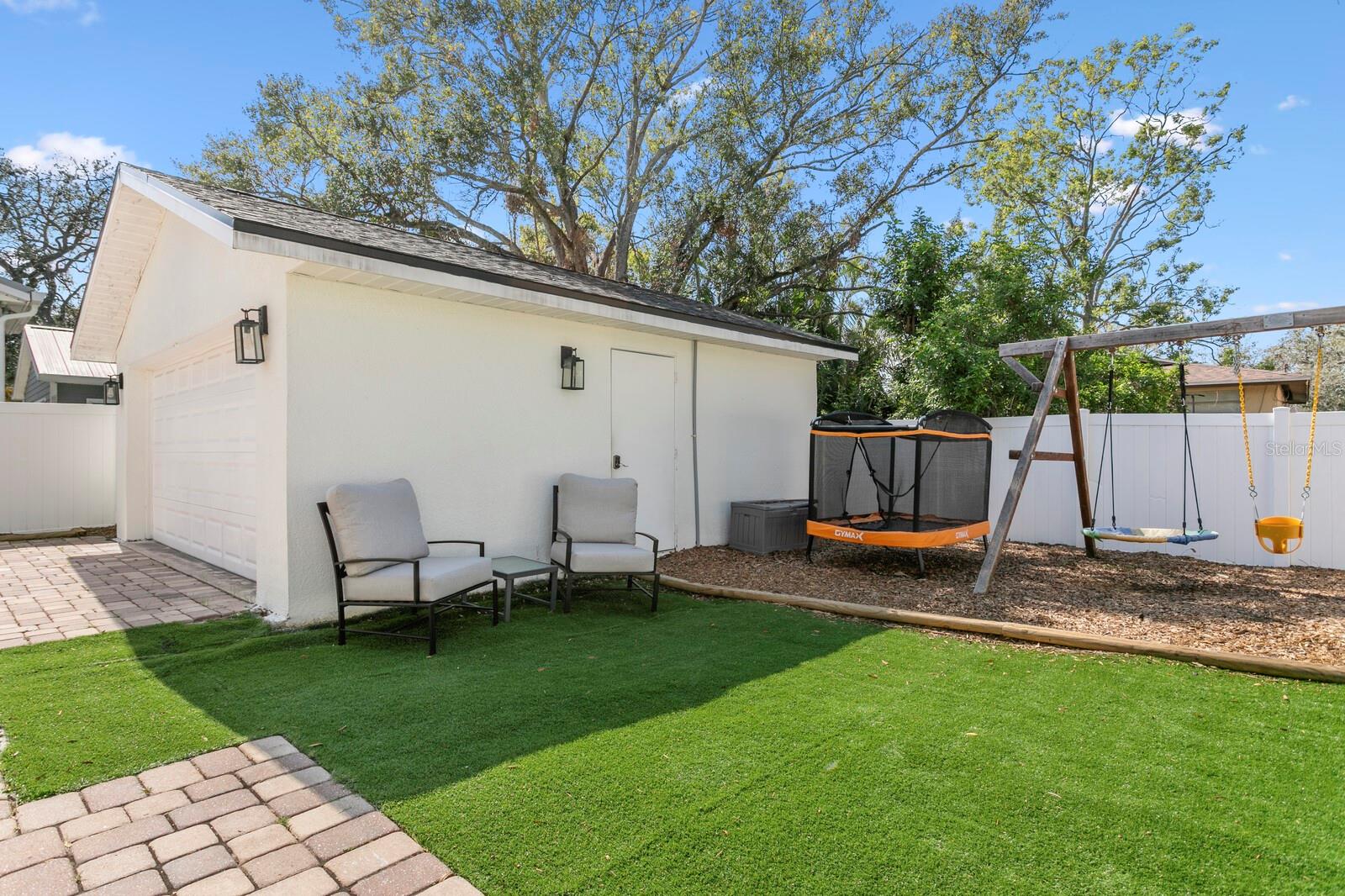 A paver patio leads to the artificial turf backyard