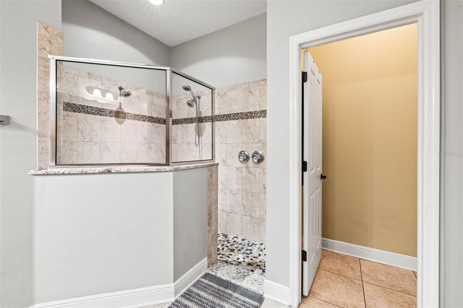 Primary bathroom features a private toilet area as well as a walk in shower with multiple shower heads.