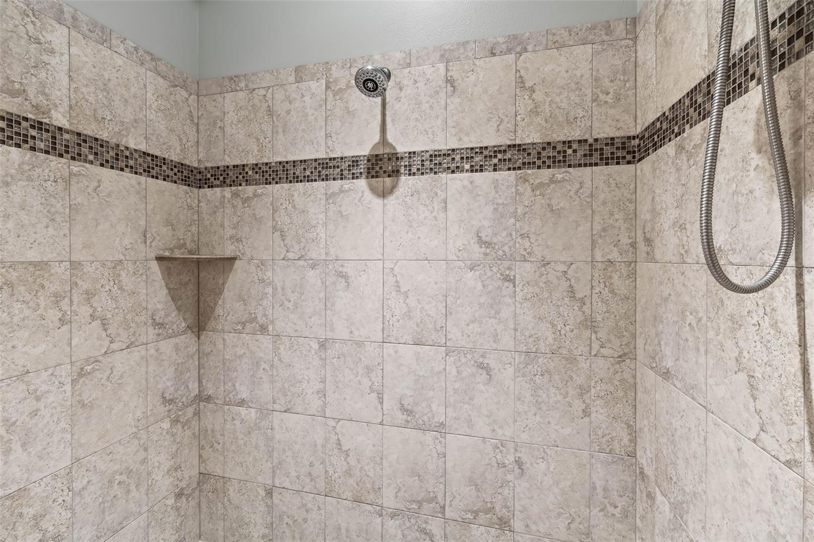 Primary bathroom shower featuring multiple shower heads and decorative tile.