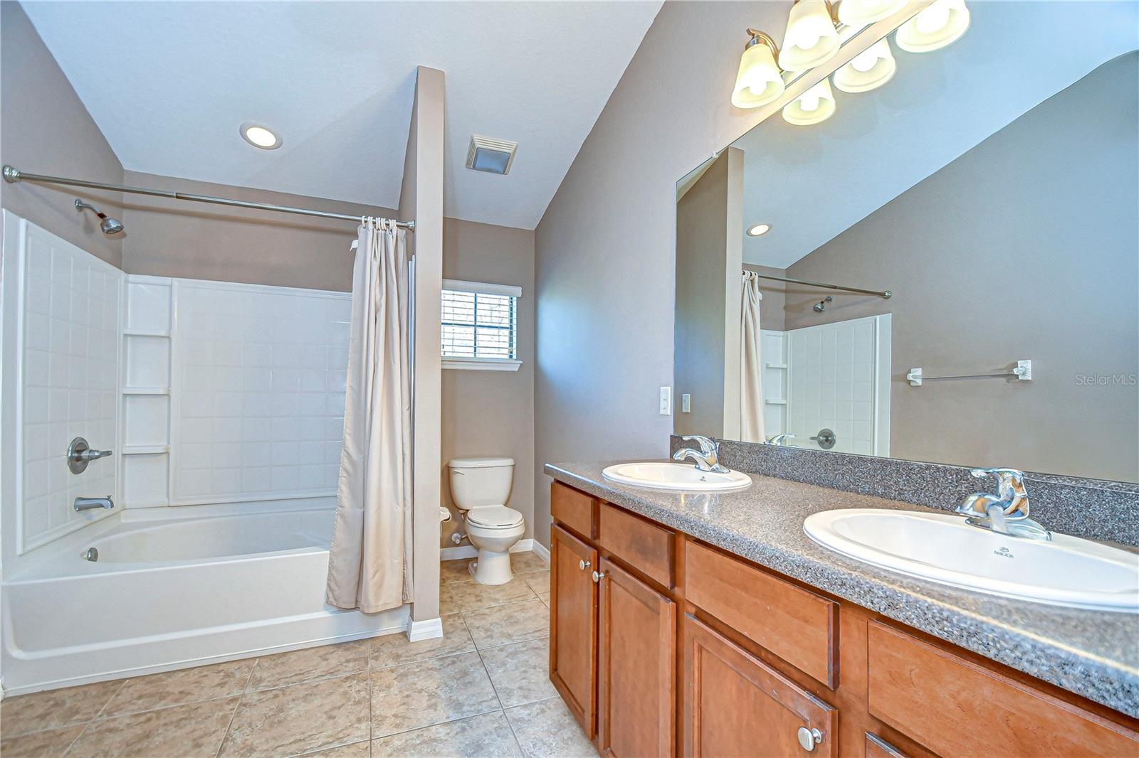 Spacious primary bathroom featuring dual sinks, a chic granite countertop, and a shower-tub combo ready for relaxation.