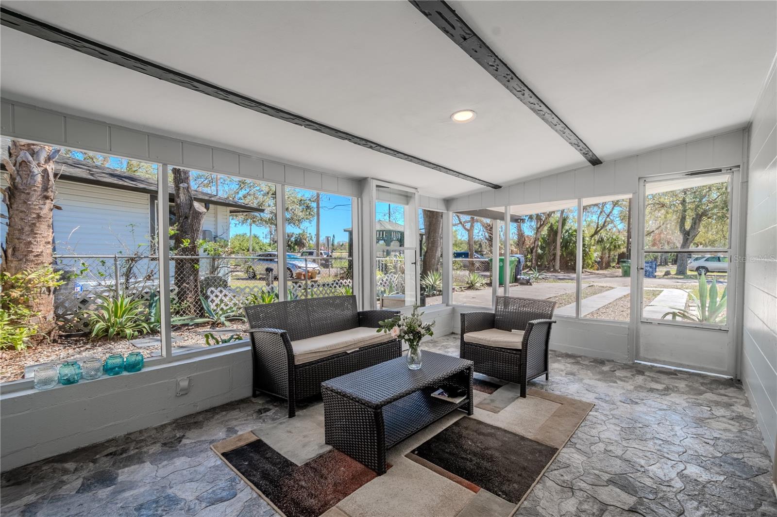 A lovely Florida sun room with stone flooring, recessed lighting and beam accented ceiling.