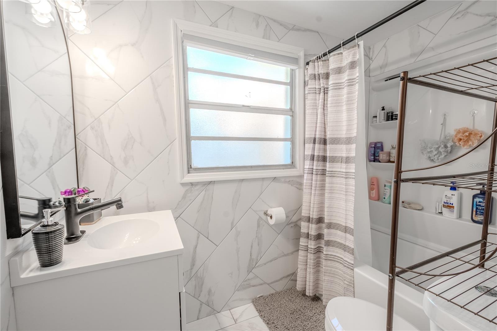 The updated bathroom features tile floor and walls, a tub with shower and a mirrored vanity with storage.