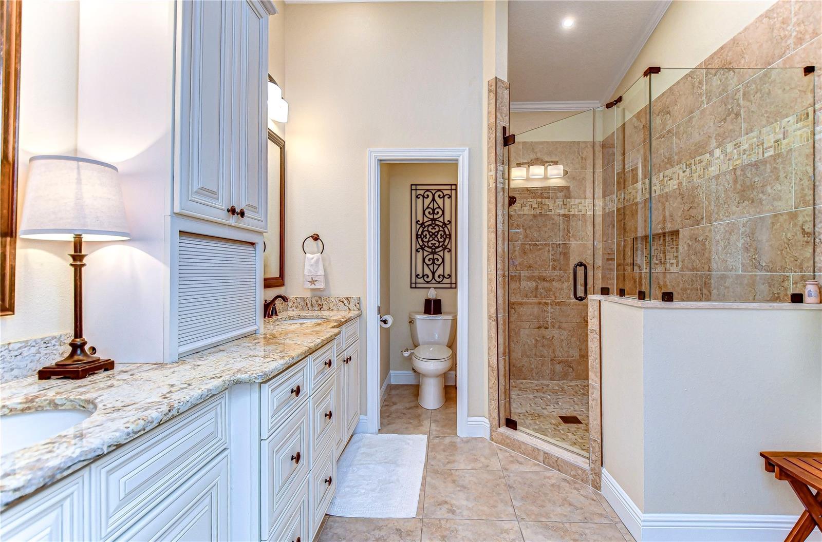 Start your day in style with this luxurious primary bathroom, showcasing elegant granite countertops, stunning cabinetry, and a spacious glass-enclosed shower