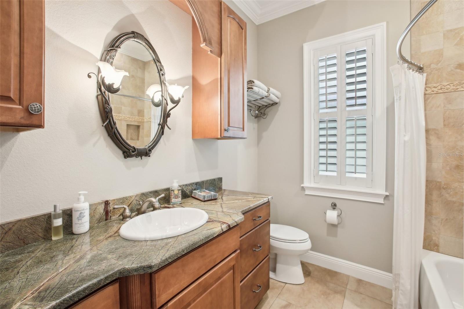 Gorgeous guest  bathroom with beautiful granite, cabinets and tiled shower with bathtub