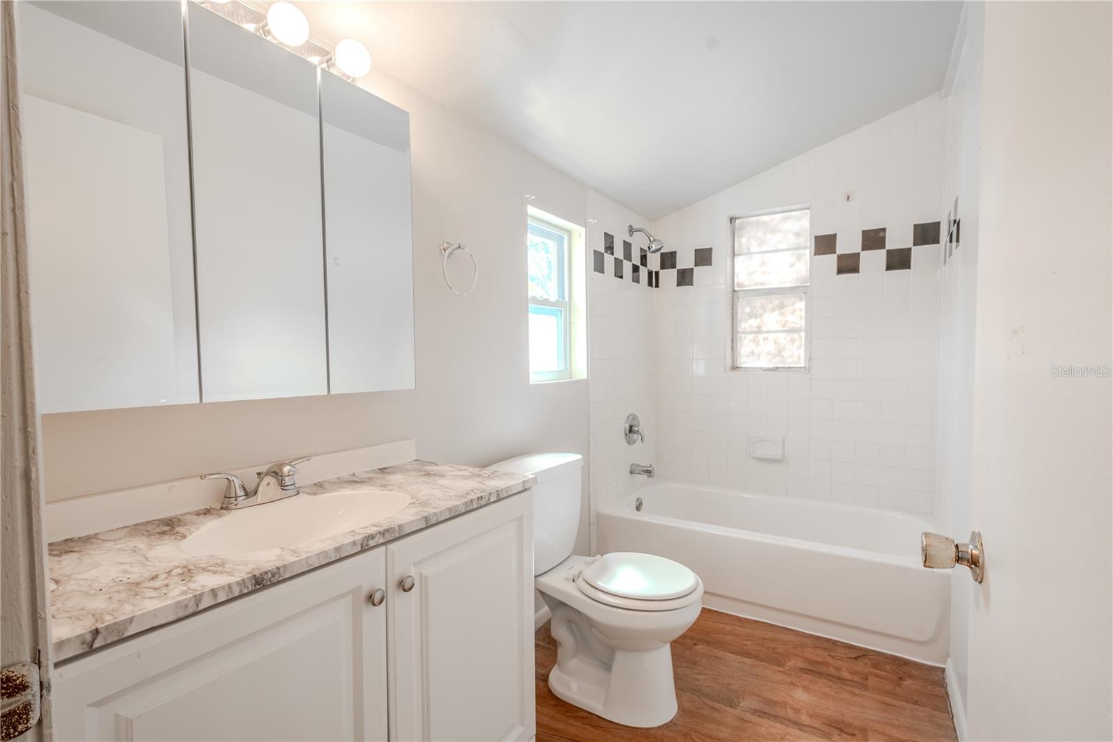 Unit 2 - bathroom has laminate flooring, a mirrored vanity with storage and a tiled tub with shower.