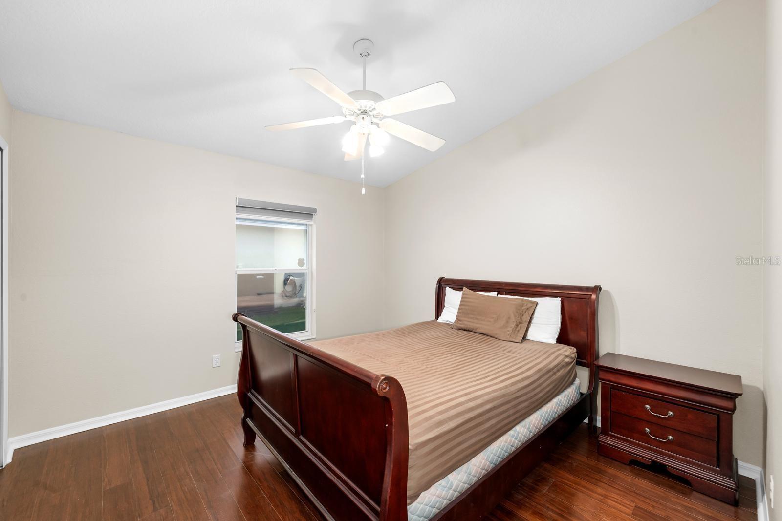 Bedroom 2 has a newer lighted ceiling fan, bamboo wood flooring, and a window shade. This bed is a queen size.