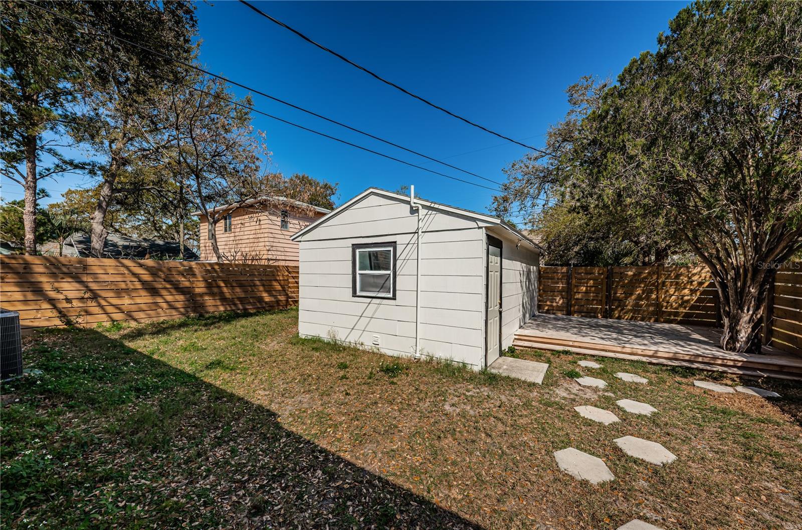 backyard with deck on right side of detached garage and fire pit on left side of garage.