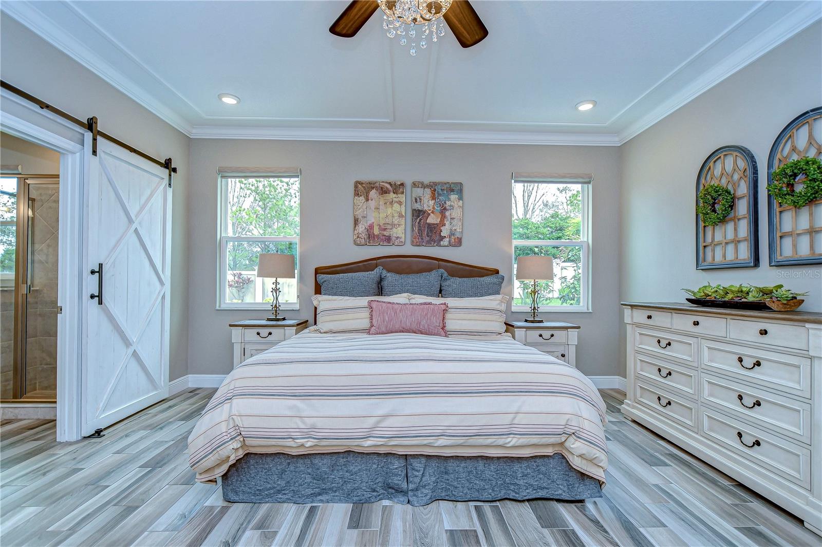 This airy primary bedroom is  adorned with elegant tray ceilings