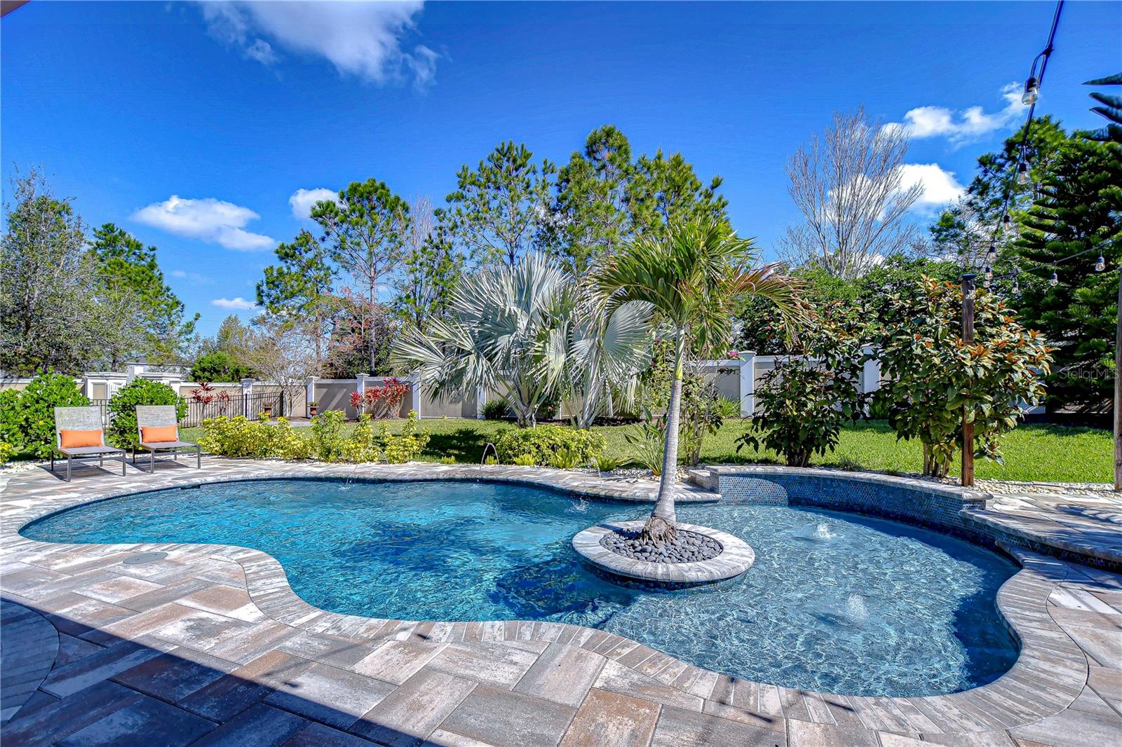 The sparkling pool, surrounded by lush greenery and elegant stonework, invites relaxation and luxurious outdoor living.