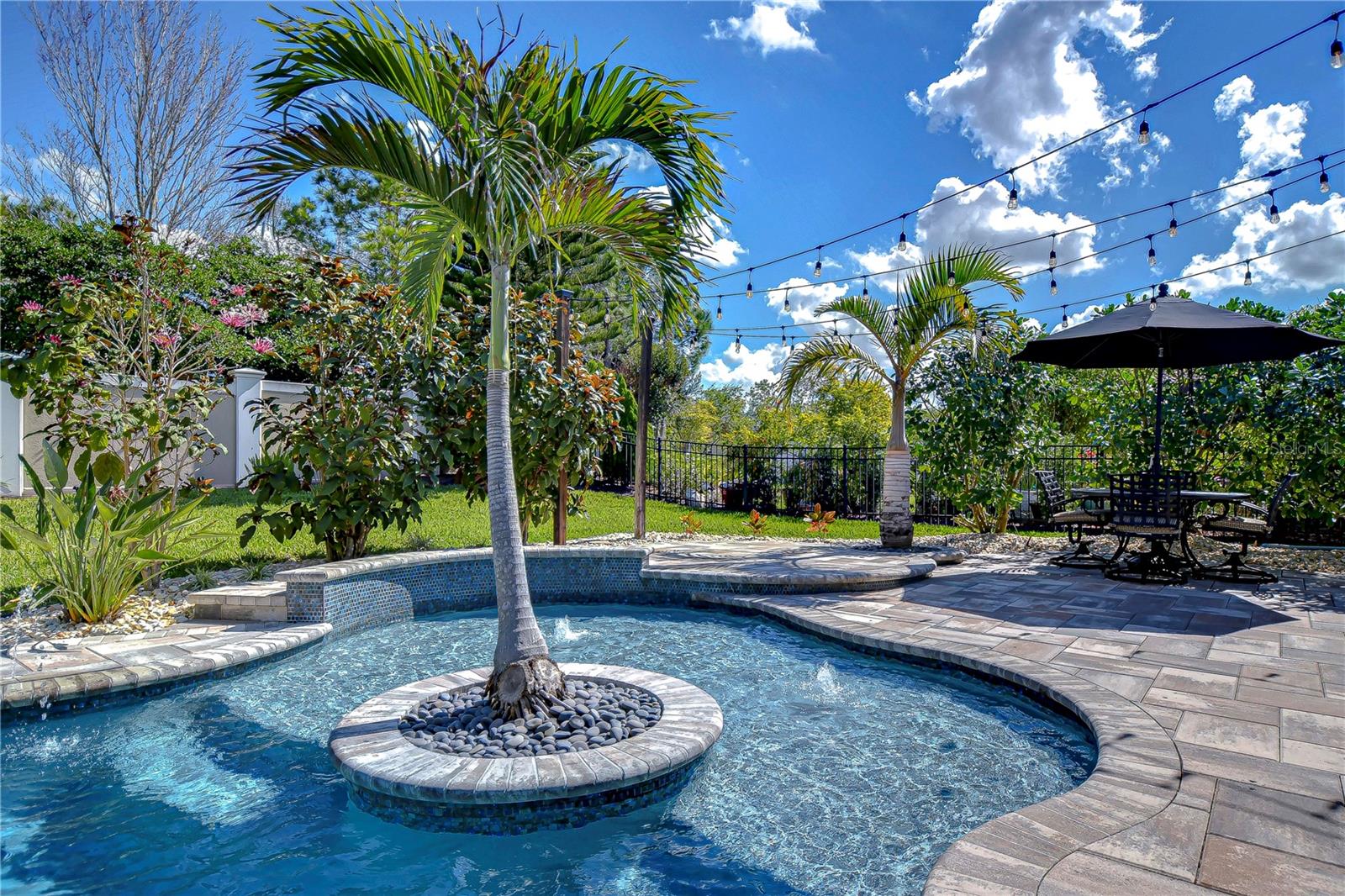 This beautifully landscaped backyard oasis, is complete with a pool surrounded by lush greenery and stylish patio lighting.