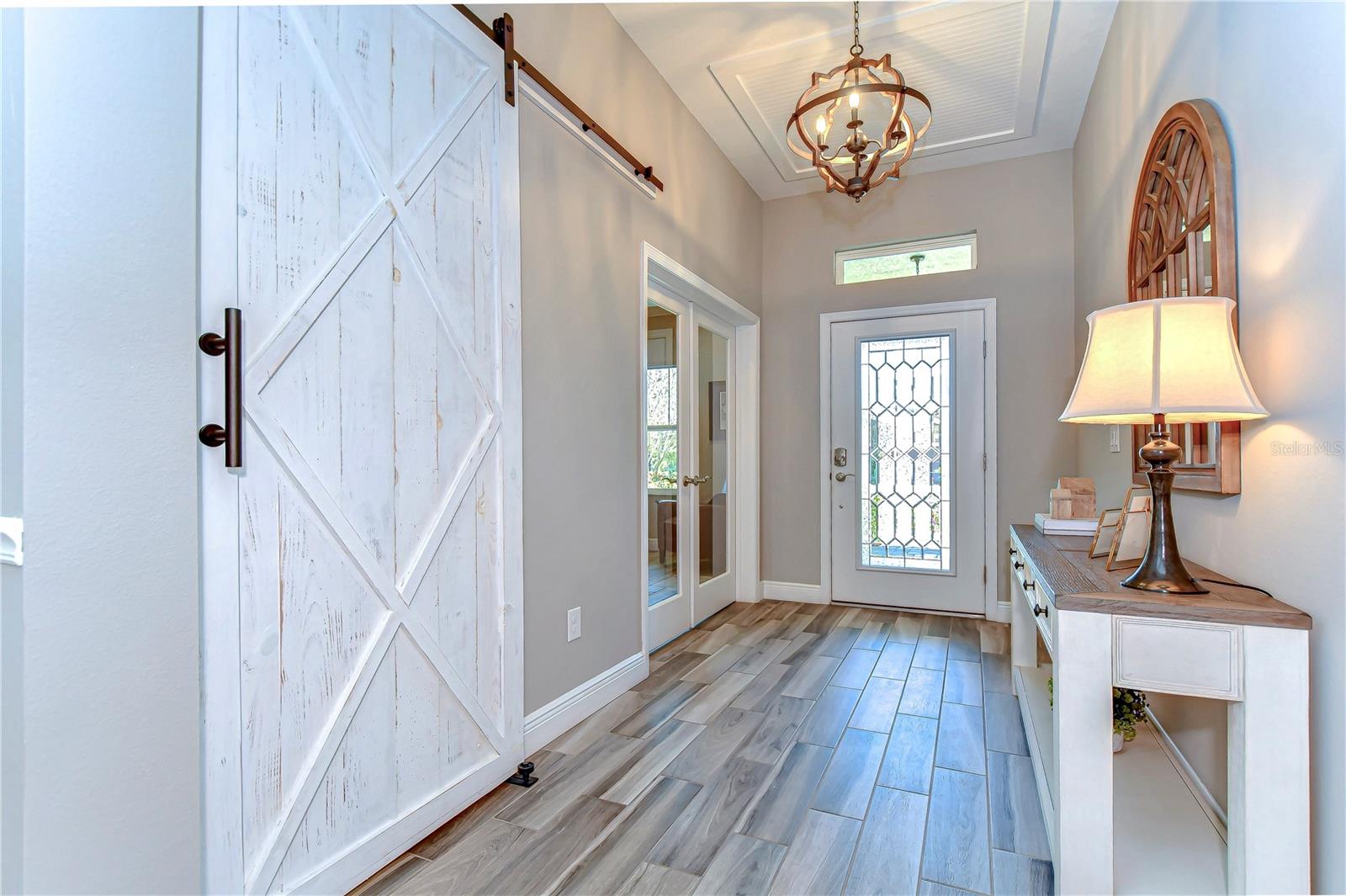 This enchanting entryway boasts a charming rustic barn door, sophisticated chandelier, and chic wood tile flooring.