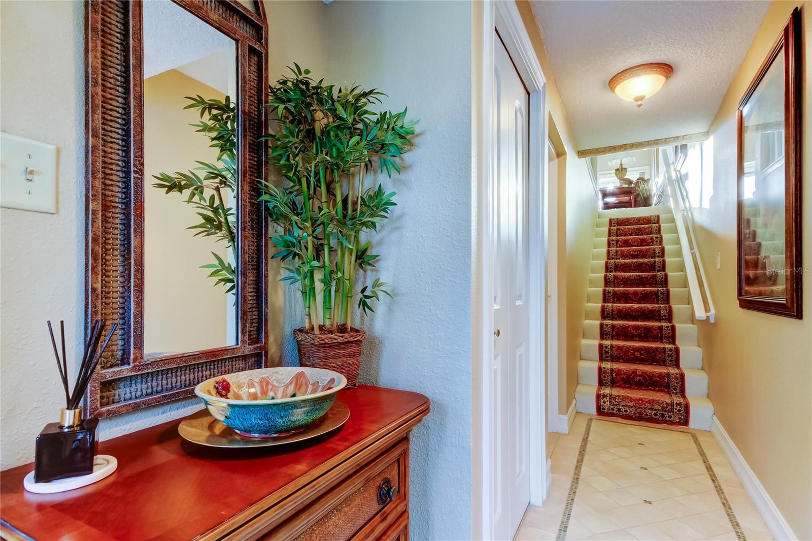 A beautifully decorated entryway featuring a stylish console, elegant mirror, and warm lighting, leading to a staircase with classic carpeting for a welcoming ambiance.