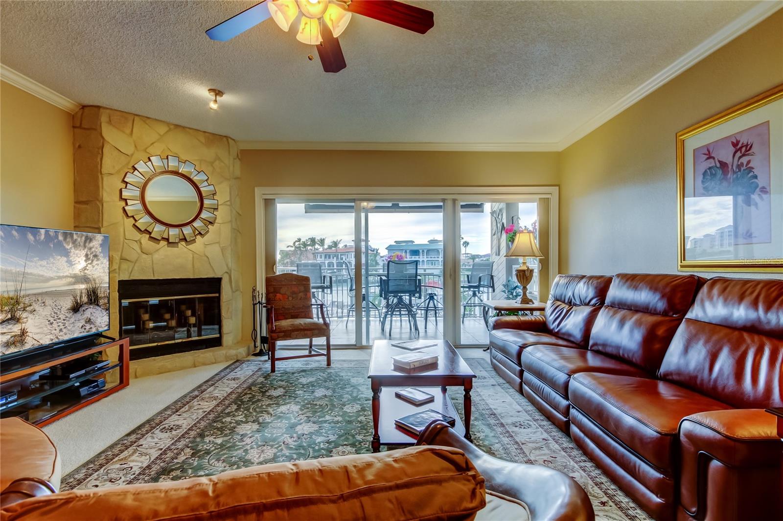 Another view of the living room showcasing its elegant design, plush leather seating, cozy fireplace, and bright natural light from the expansive sliding doors leading to the waterfront deck.