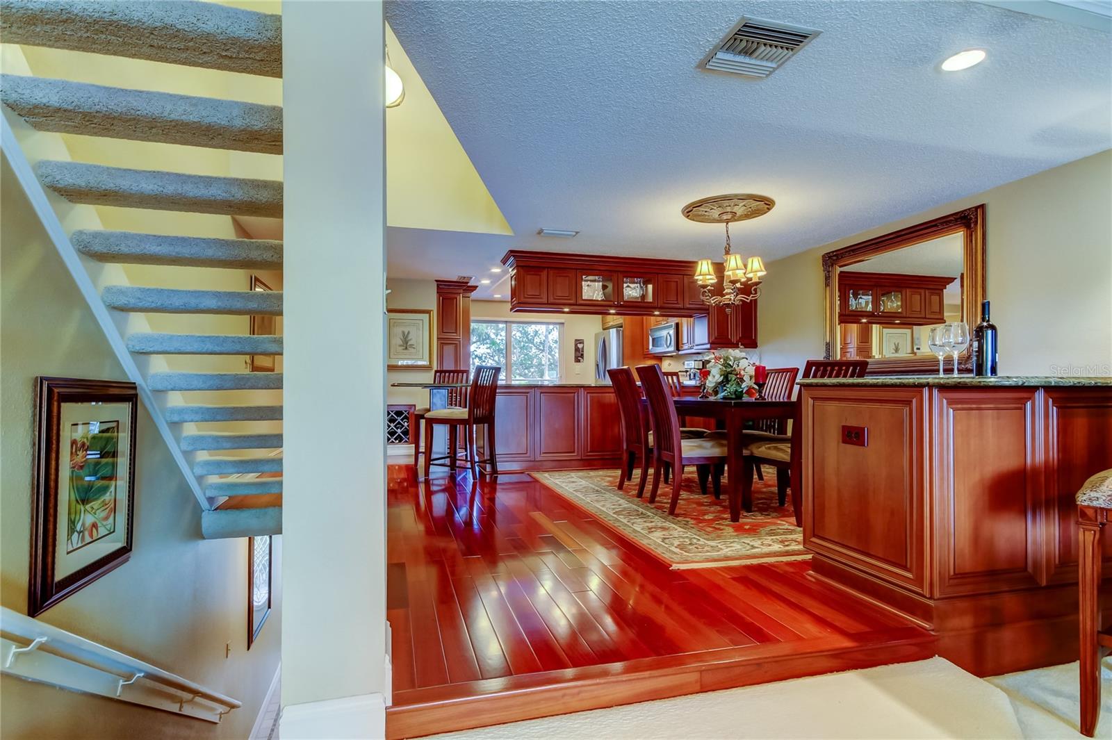 An elegant view of the dining area and kitchen, featuring rich wood cabinetry, stylish lighting, and an open layout seamlessly connected to the living space, with a modern staircase adding architectural charm