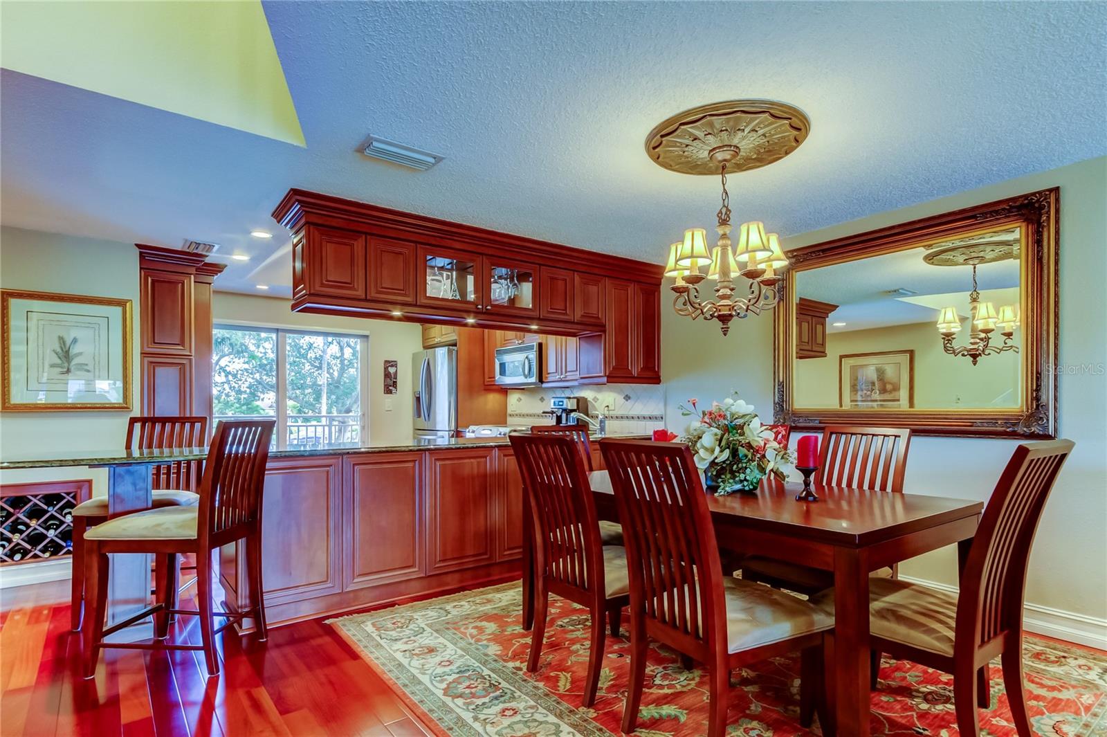 A spacious and elegant dining area seamlessly connected to the kitchen, featuring rich cherry wood cabinetry, a stylish chandelier, and a warm, inviting ambiance perfect for gatherings.