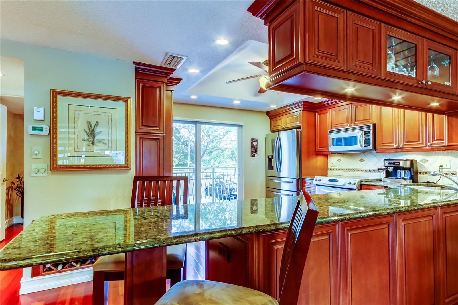 A beautifully designed kitchen with rich wood cabinetry, granite countertops, and a breakfast bar, seamlessly connecting to the outdoor balcony.