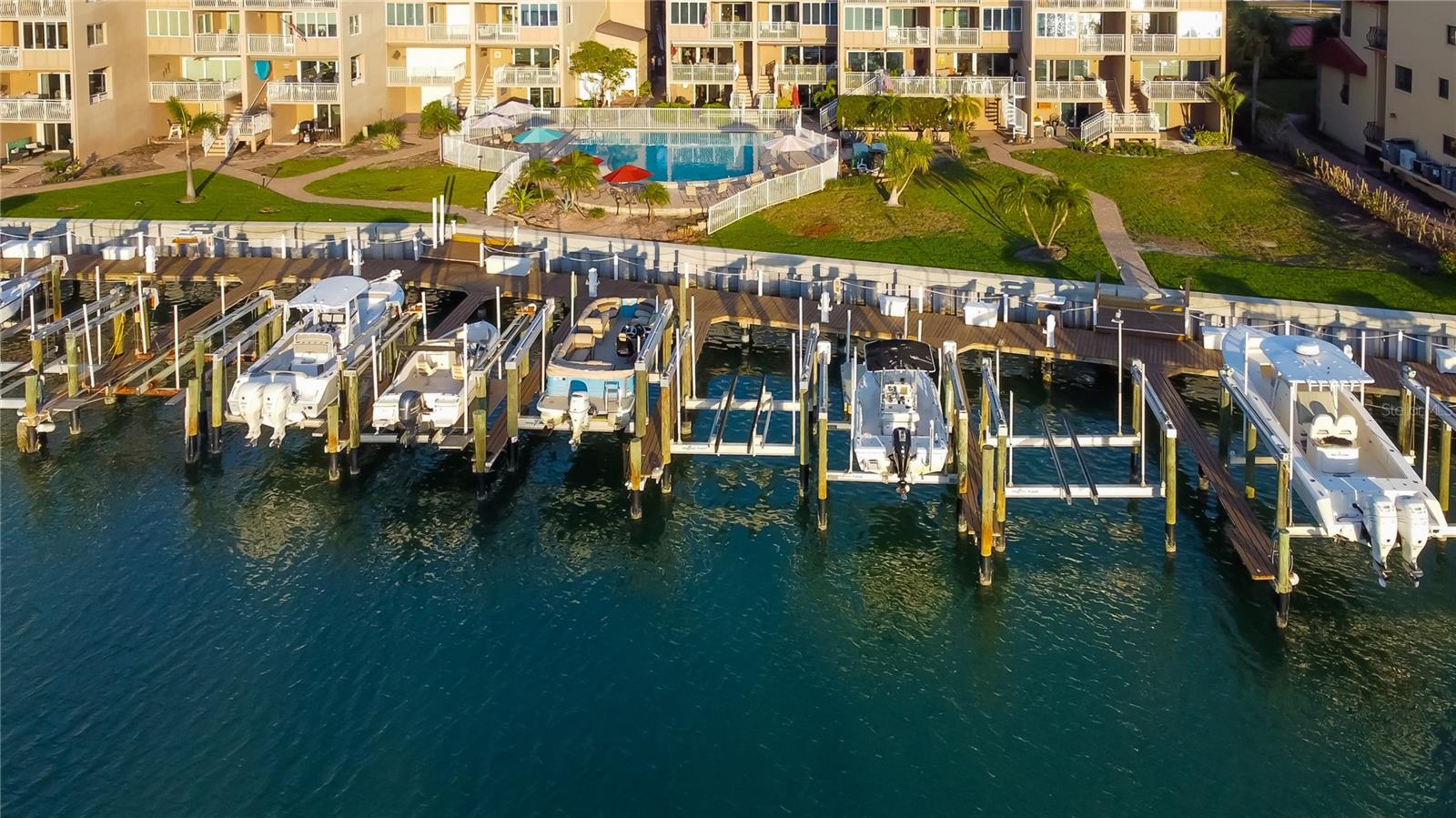 Sunlit serenity at the neighborhood marina, where boats rest on crystal-clear waters. Slip #12, the empty slip in the middle, awaits its next vessel. Extensive landscaping replacement is underway, enhancing this waterfront retreat.