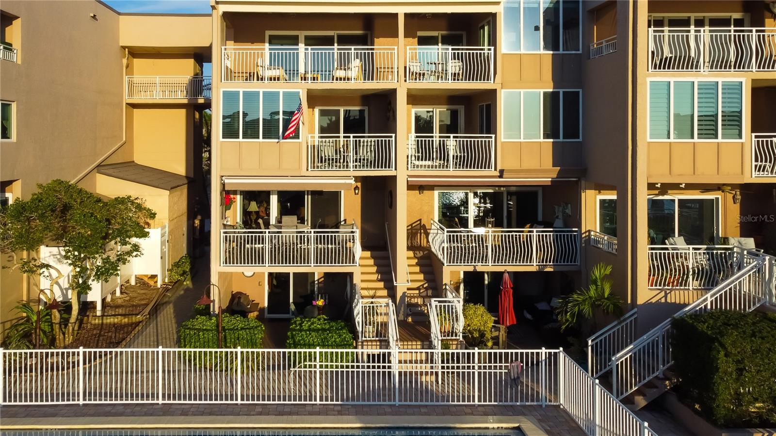 Rear view of Unit T-7, showcasing the inviting patio with a grill, two of the four spacious balconies, and an electric canopy for shaded relaxation—all overlooking the pool and waterfront.