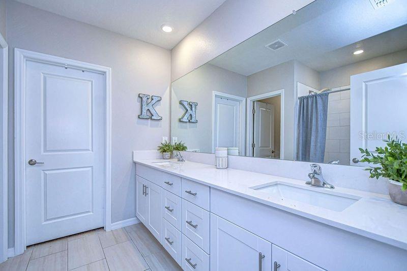 Double sink vanity in primary bathroom with door to large walk in closet