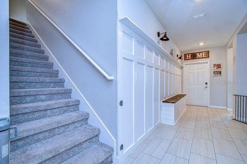 Stairs to second floor with view toward front door and upgraded accent wall with bench accented with cypress bench seat.