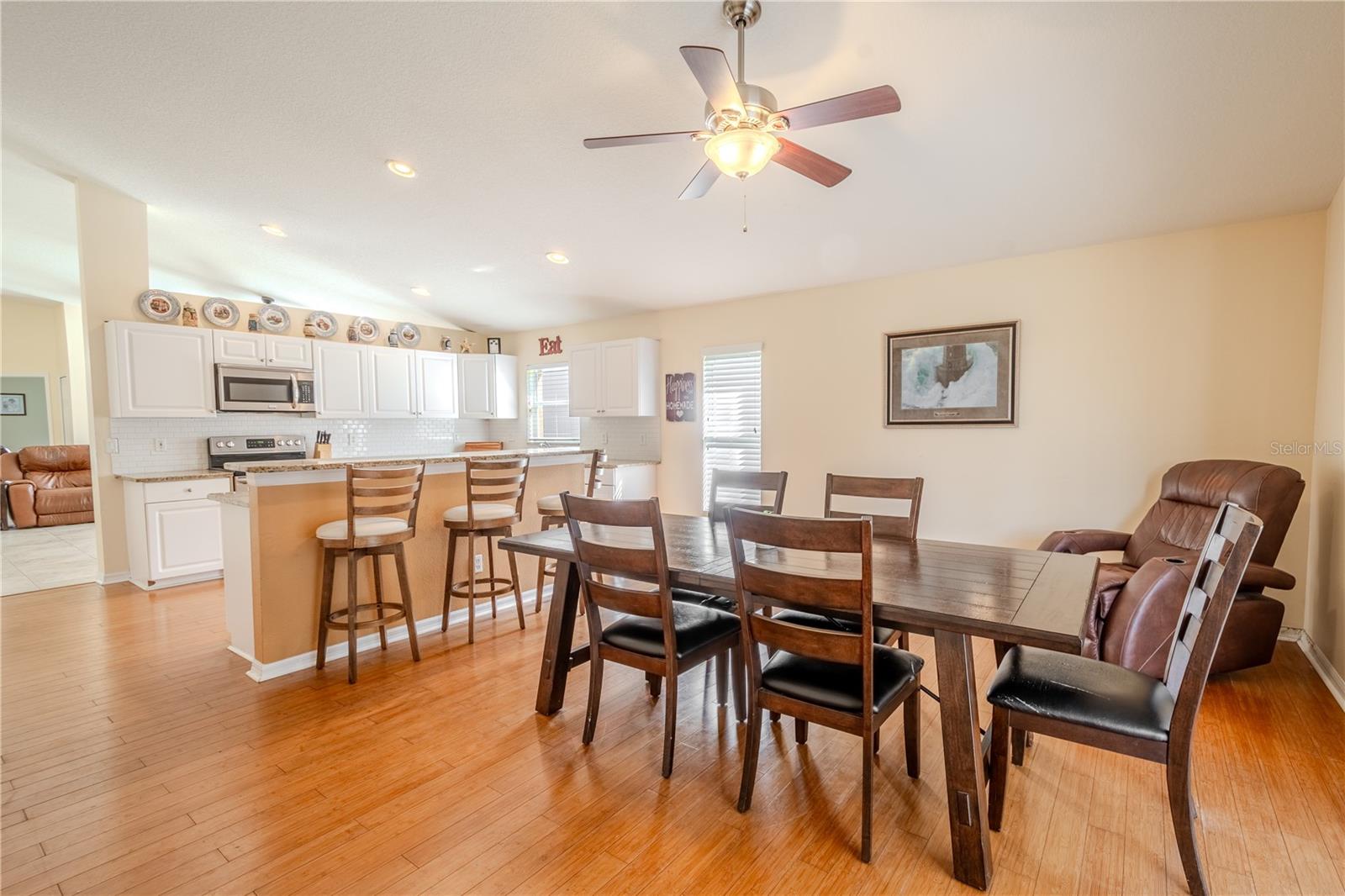 The family room (currently used as a dining area) has wood floors, neutral tones and a ceiling fan with light kit.