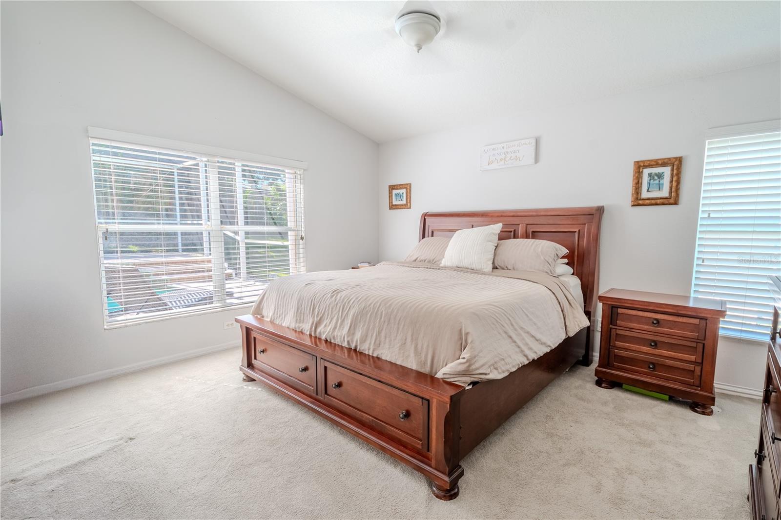 The primary bedroom features neutral tones, carpet, a ceiling fan with light kit, an ensuite bath, a walk-in closet and a view of the pool.