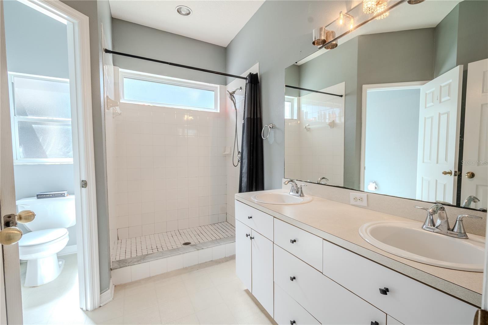 The primary bathroom features a step in shower, a private water closet, and a mirrored, dual sink vanity with storage.