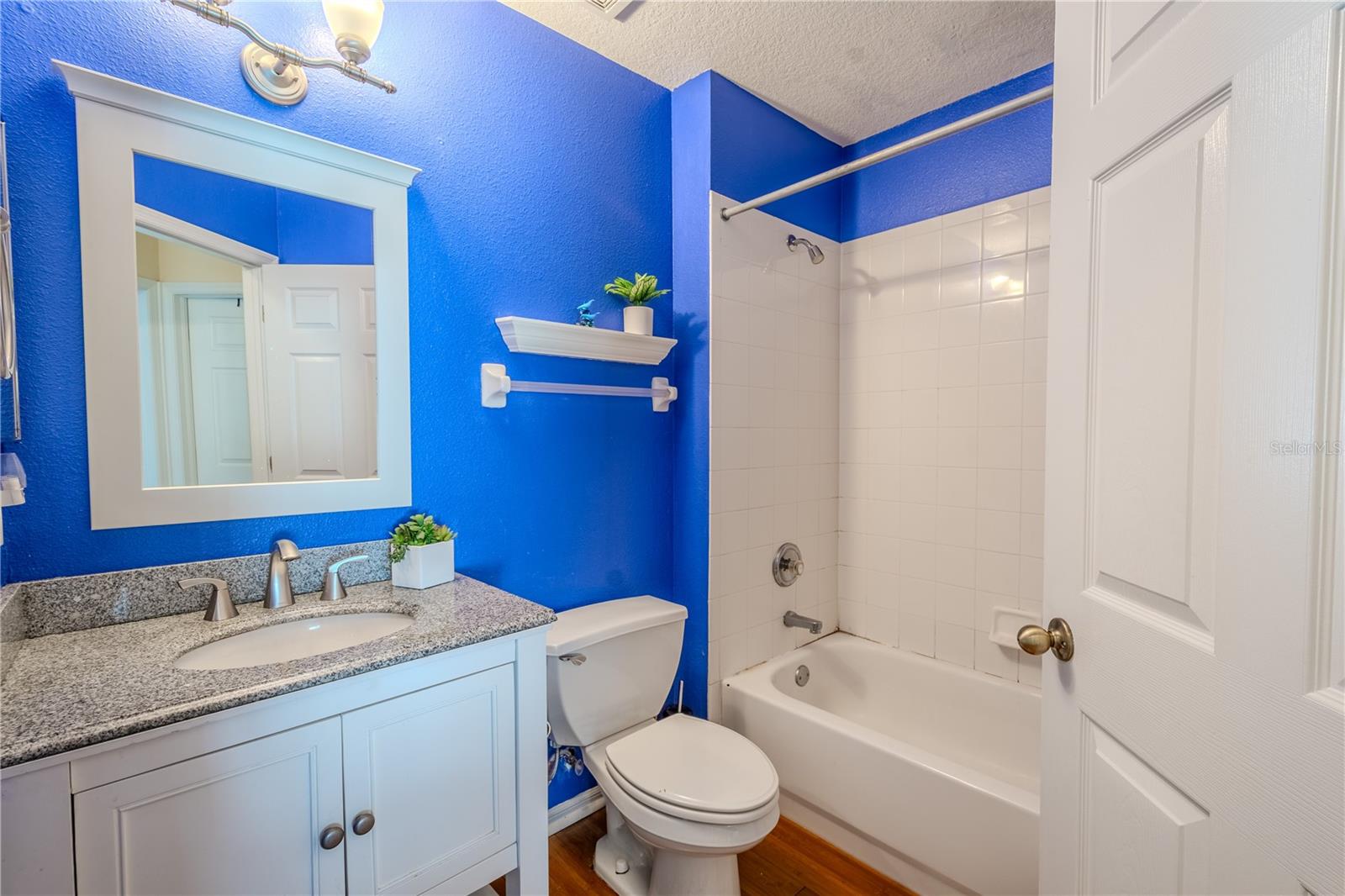 Bathroom 2 features a  tub with shower, a mirrored vanity with uplight fixture and storage.