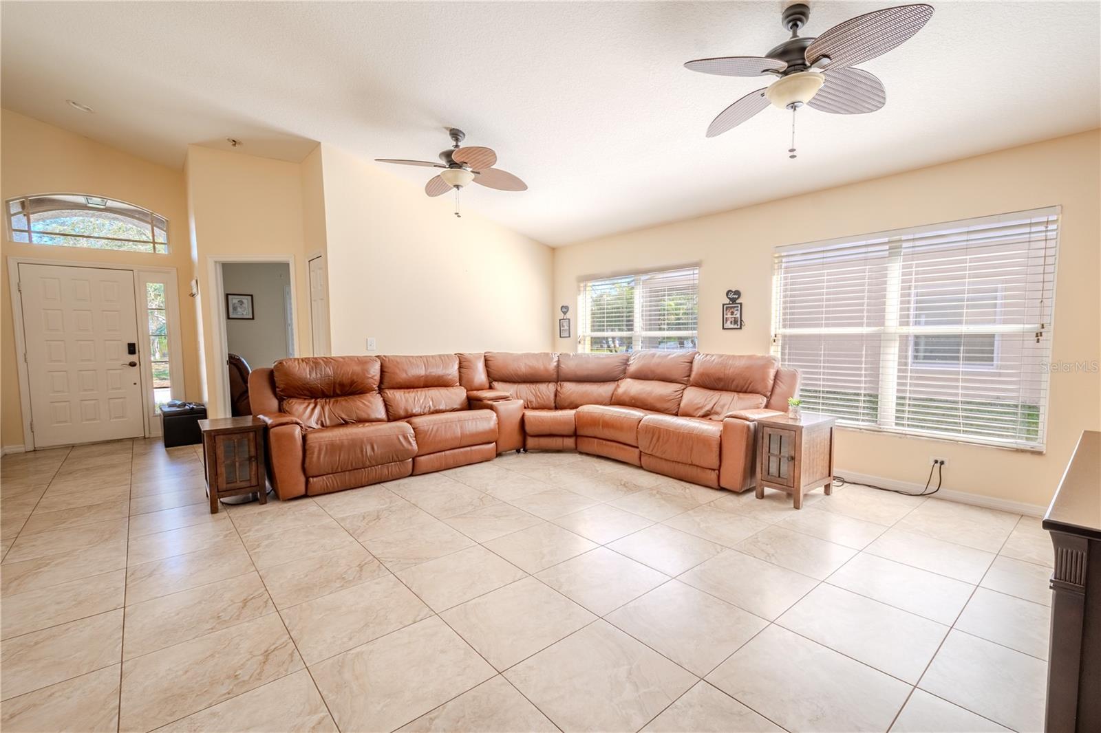 The living room features tile flooring, vaulted ceiling, neutral tones and two ceiling fans.