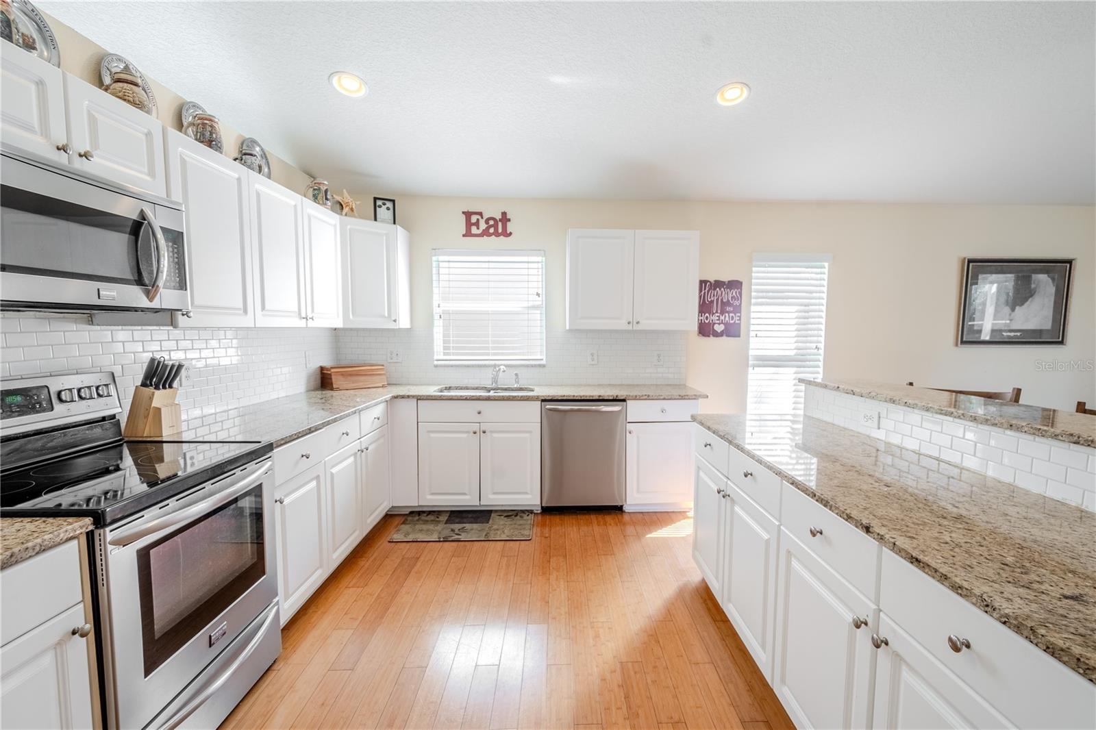 The spacious kitchen features wood plank flooring, white cabinetry with subway tile backsplash and granite countertops.