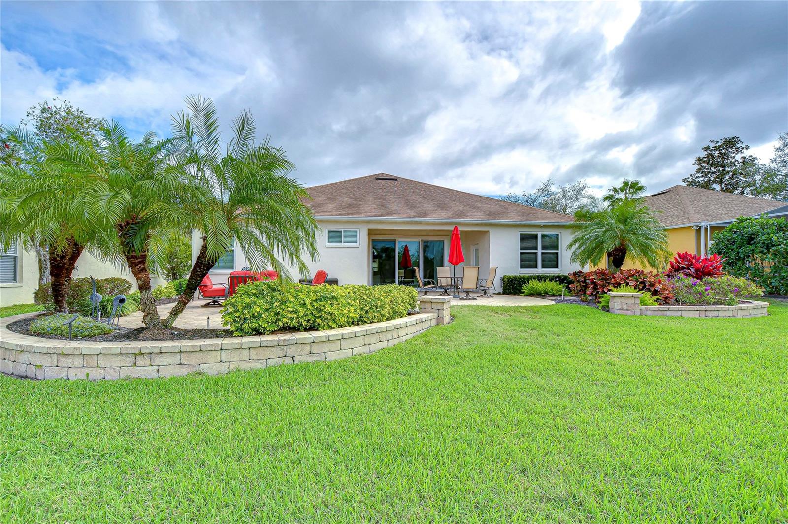 This lush backyard invites relaxation with its tropical landscaping, spacious patio, and vibrant accents.