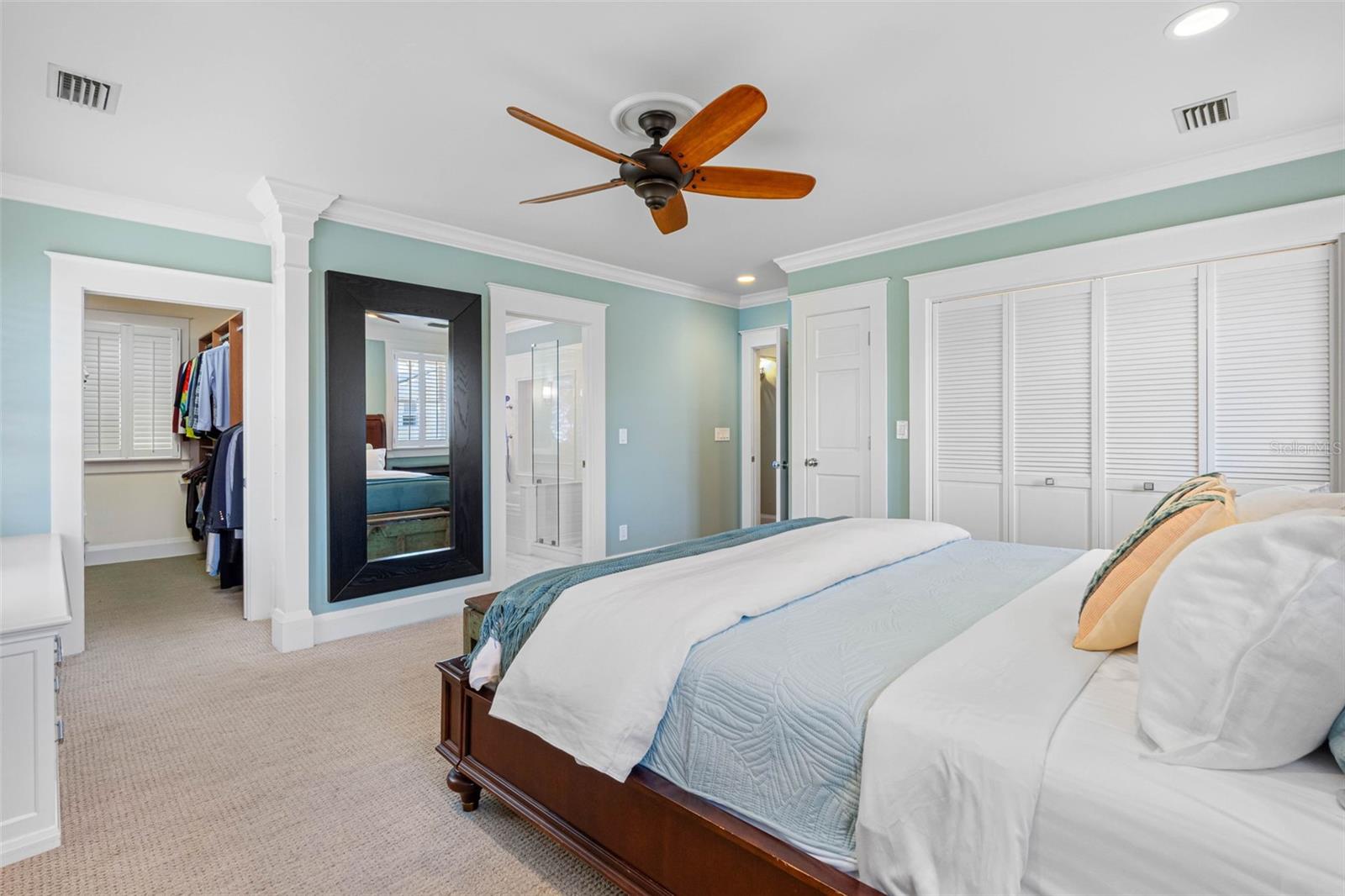 The en suite master bedroom features a  walk in closet, built-ins, additional closets, plantation shutters, and a ceiling fan.