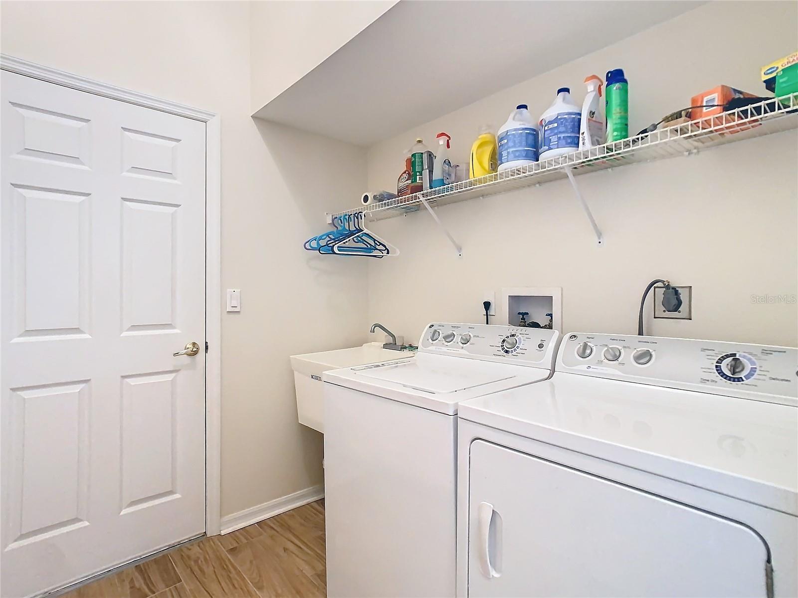 The laundry area is on upgraded ceramic tile. There is a deep sink as well. Washer and dryer stay with the property. Shelving above for storage of your laundry cleaning needs. The door opens into the 2 car garage.